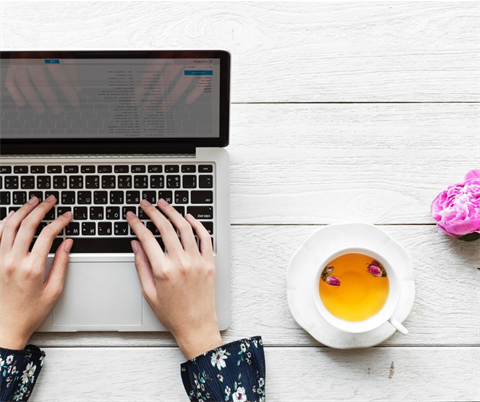 Female hands typing on a laptop with a cup of tea sitting next to the right hand