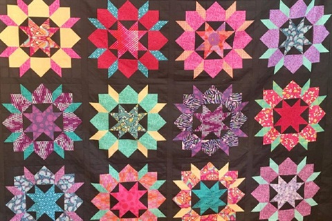 A patchwork quilt with a black background and strong coloured pieces