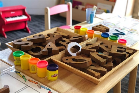 Photo of a desk in a preschool covered in wooden block letters and tubs of paint