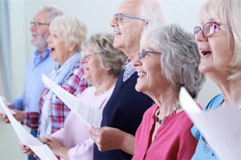 Photo of six older people holding sheet music, singing and smiling