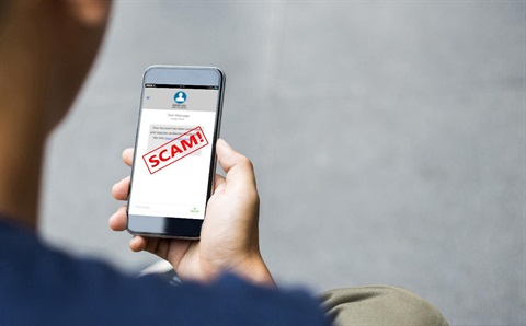 Person holding mobile phone with SCAM written on the screen in red writing