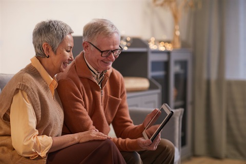 A couple sitting on a couch, looking at a tablet