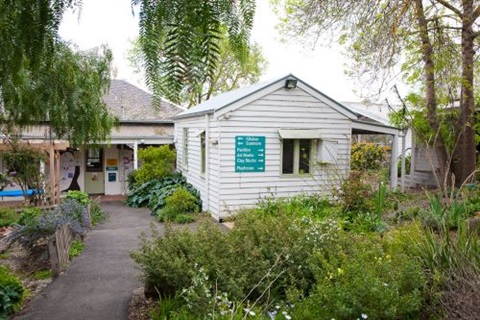 Photo of the Living & Learning centre in Eltham. It is a white weatherboard building surrounded by a cottage garden