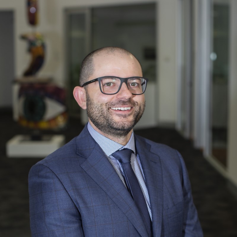 Photo of Vincenzo Lombardi. Vincenzo is wearing a suit and tie and standing in the foyer of the Nillumbik Council building.