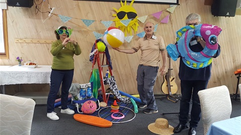 Photo of three people holding a variety of props such as a beach ball, novelty sunglasses, hats etc