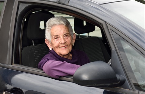 A senior woman sitting in the driver's seat of a car.