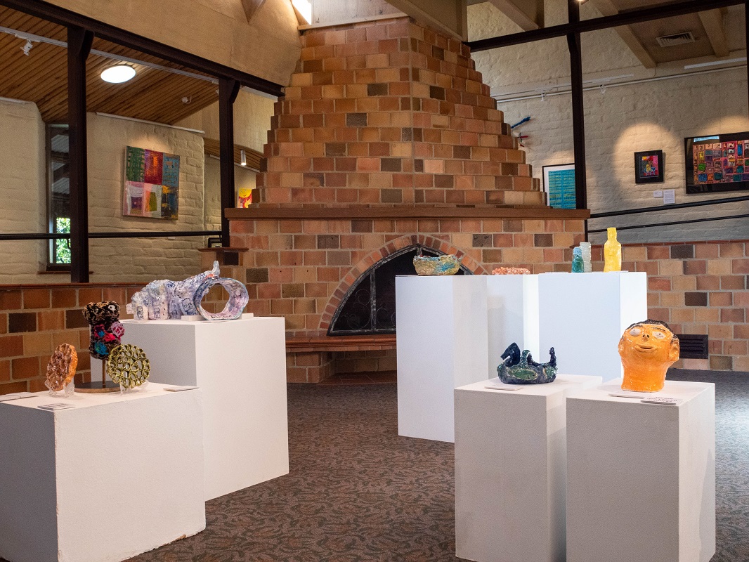 Photo of Art and Agency exhibition by Araluen, depicting ceramics works on plinths and 2D works on wall on ramp of gallery.