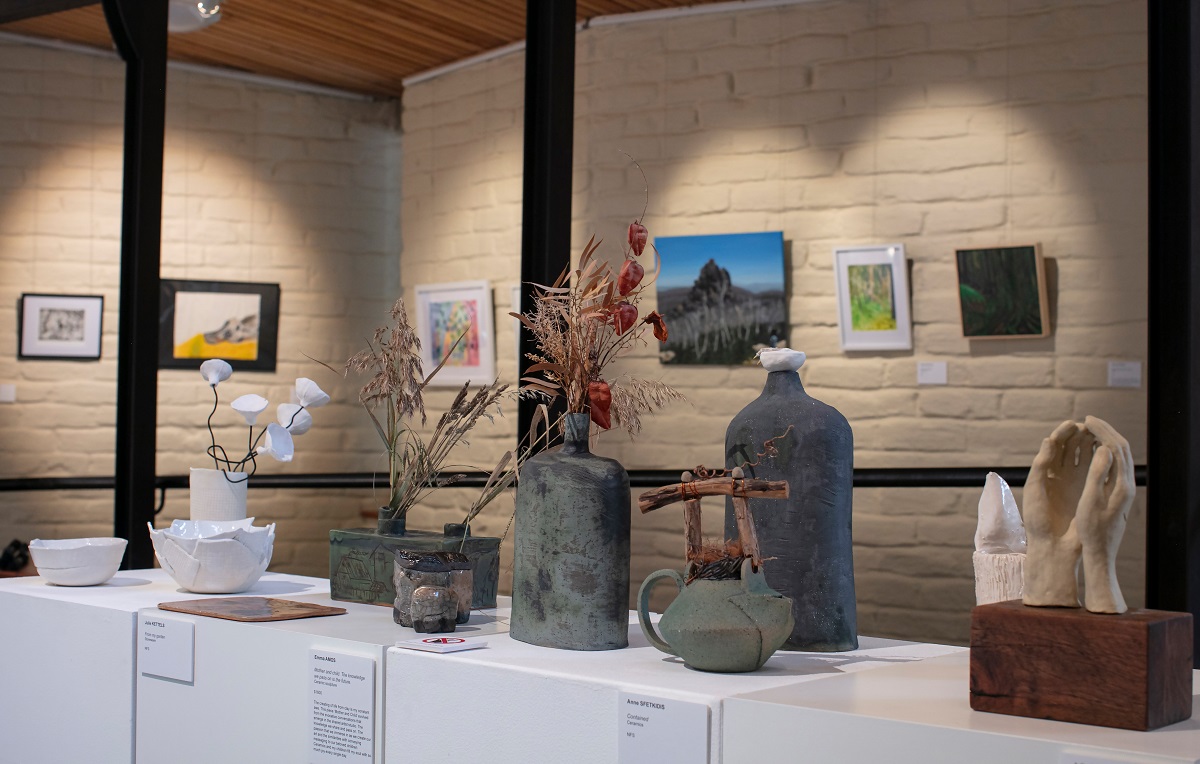 Photo of sculptural works on white plinths and two dimensional works on hung behind on the mudbrick wall