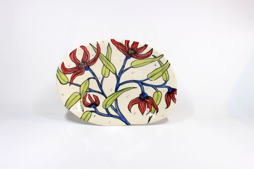 Visual description: A ceramic plate with five red flowers with blue stems, and light green leaves. With a cream background with small blue dots. 