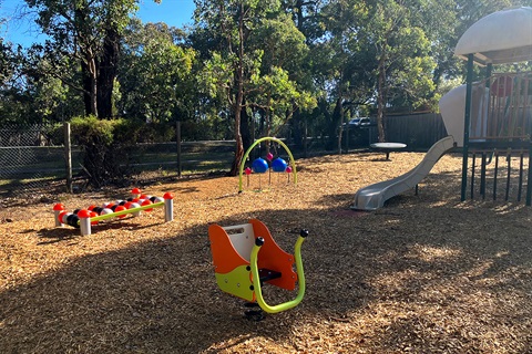 A yellow and orange swinging seat sits in front of play equipment