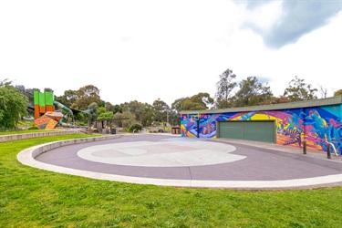 A large paved area sits in front of a brightly coloured building, a playground is in the background