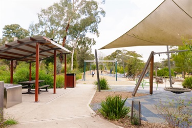 A roof shades a table and chairs and a shade sail covers a swing