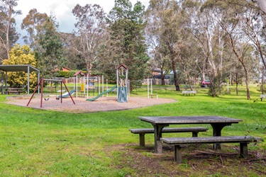 A picnic table on the grass in front a children's playground and tall trees.