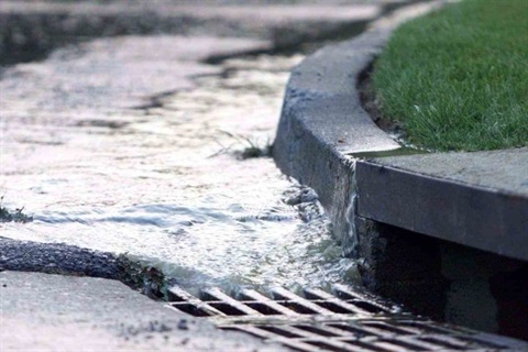 Photo of water rushing into a stormwater drain on the curb of a street