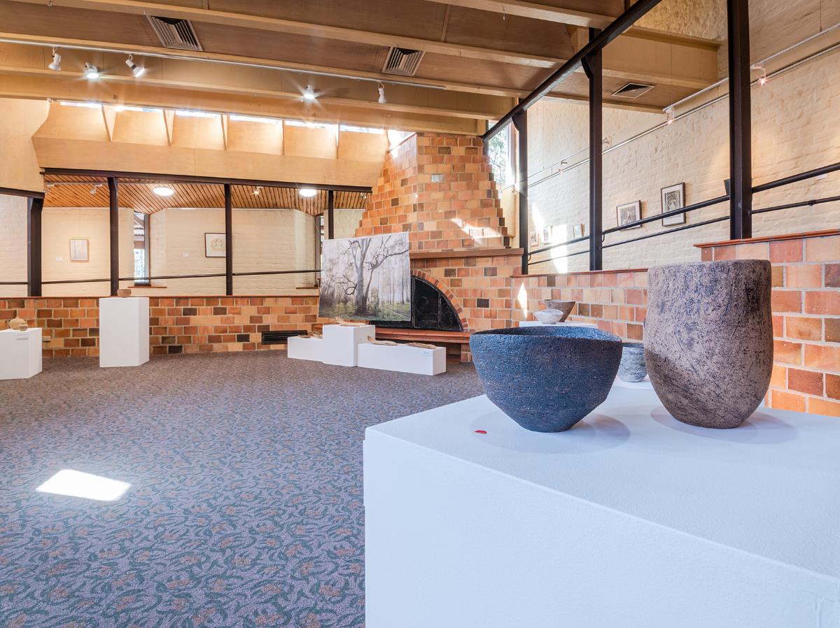 Photo of ceramics on plinth and print in front of fireplace installed in the Eltham Library Community Gallery 