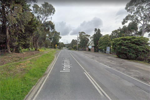 Photo or Ironbark Road Yarrambat, looking west. A bitumen road with buildings and trees.